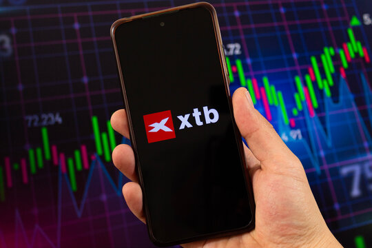 macro photo of a male hand with xtb logo inside a smartphone with blurred stock market at background