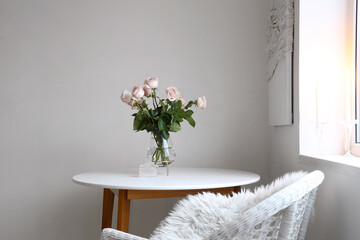 Vase with beautiful rose flowers on table near light wall