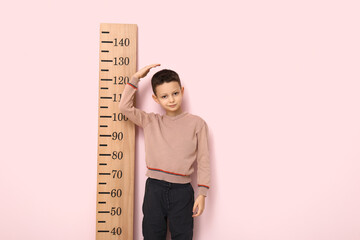 Cute little boy measuring height on pink background