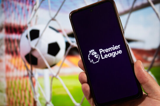 a smartphone with uk football premier league logo and blurred stadium and football ball at background