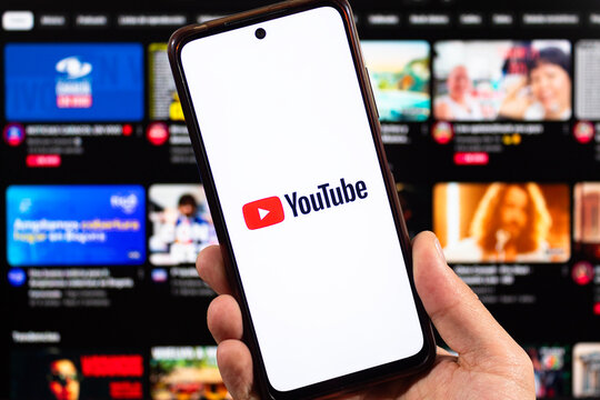 A male hand holding a smartphone with his right hand and youtube logo with blurred youtube interface at background
