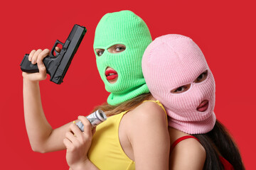 Beautiful young stylish women in balaclavas and swimsuits holding money with gun on red background