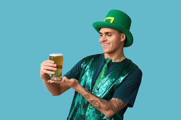 Happy young tattooed man in green clothes and with glass of beer on blue background. St. Patrick's...