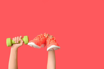 Female hands with dumbbell and shoes on red background, closeup