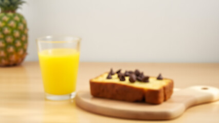 A simple breakfast of banana bread with chocolate chips and pineapple juice. Natural lighting highlights the textures, set on a light wood table with a white wall backdrop.