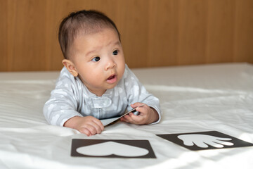 5 month old baby playing with picture cards on the bed in the morning.