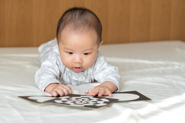 5 month old baby playing with picture cards on the bed in the morning.