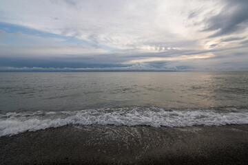 An incoming wave on the Black Sea and a pebble beach on the Sochi coast on a summer day with clouds, Sochi, Krasnodar Territory, Russia
