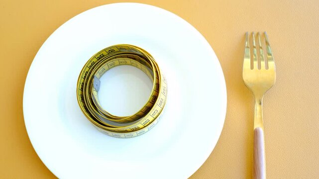 Empty plate with measuring tape and fork on brown background, intermittent fasting concept.