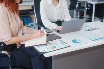 Obraz premium Two Caucasian women work in an office, happily using laptops and computers at a desk, discussing financial projects, analyzing financial statements,collaborating in a meeting to ensure effective