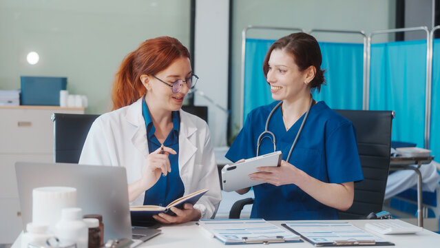 Two Caucasian female doctors work at a desk, meeting and discussing patient treatment while using a medical program modern technology in a hospital to ensure effective healthcare medicine management