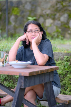 Asian woman sitting outside her village house enjoying the breeze and natural beauty of tropical rice fields