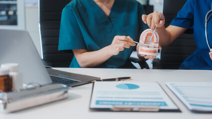 Two Asian female doctors meet at a table in a clinic, with a dentist explaining dental...