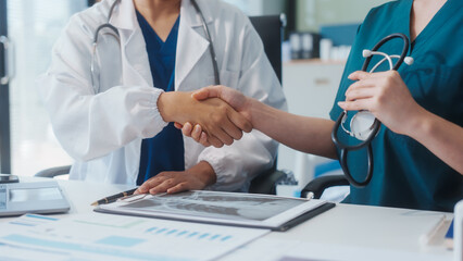 Two Asian female doctors shake hands after a successful meeting at a hospital, celebrating...