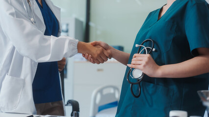 Two Asian female doctors shake hands after a successful meeting at a hospital, celebrating cooperation between two hospitals and recognizing their teamwork in advancing healthcare and patient care
