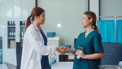 Two Asian female doctors shake hands after a successful meeting at a hospital, celebrating cooperation between two hospitals and recognizing their teamwork in advancing healthcare and patient care