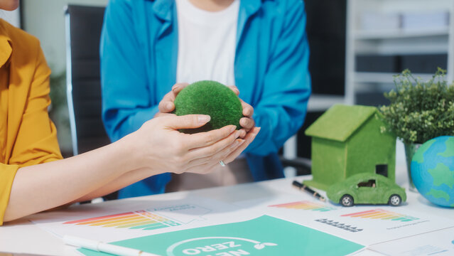 wo Asian business woman work at a desk,using a laptop for an ESG presentation on screen,discussing sustainability,green energy, recycling,net-zero strategies to promote environmental responsibility