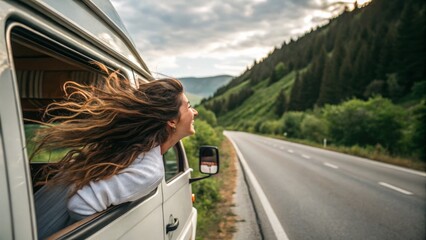 A woman enjoys the breeze while leaning out of a van window, surrounded by lush greenery and a winding road under a cloudy sky.