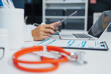 Fototapeta premium Asian female doctor is reviewing medical records, working on a computer, planning treatment, giving online consultations, and explaining medications to patients via a medical video call in a clinic