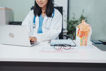 An Asian female doctor uses a respiratory system model while working on a computer, planning treatment,consulting online, explaining respiratory care to patients via a medical video call in a clinic