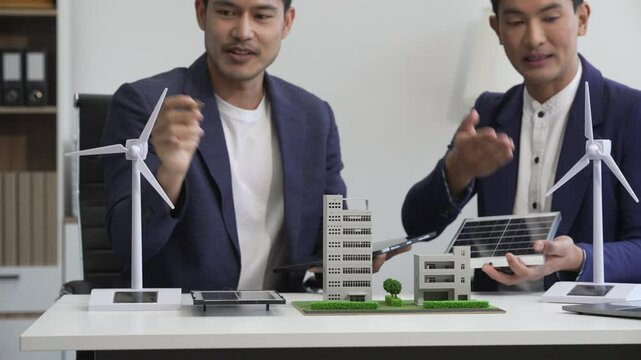 Two Asian businessmen meet at the table with wind power engineers to discuss renewable energy solutions. They exchange ideas on wind turbines, solar energy,simulations for sustainable development