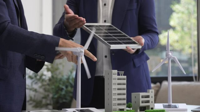 Two Asian businessmen meet at the table with wind power engineers to discuss renewable energy solutions. They exchange ideas on wind turbines, solar energy,simulations for sustainable development