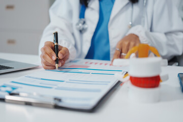 Asian female doctor uses a model of a lumbar disc to work with a computer, plans treatment,...