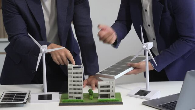 Two Asian businessmen meet at the table with wind power engineers to discuss renewable energy solutions. They exchange ideas on wind turbines, solar energy,simulations for sustainable development