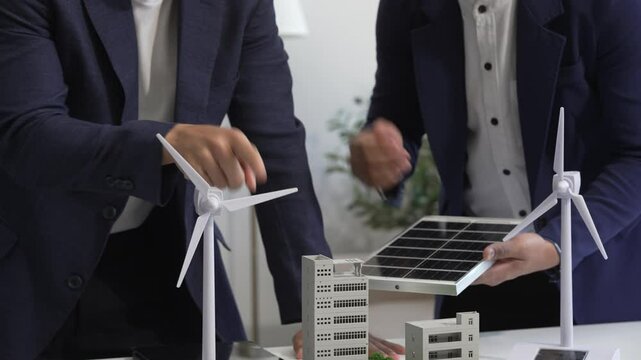 Two Asian businessmen meet at the table with wind power engineers to discuss renewable energy solutions. They exchange ideas on wind turbines, solar energy,simulations for sustainable development