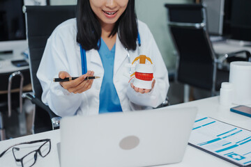 Asian female doctor uses a model of a lumbar disc to work with a computer, plans treatment, provides online consultation, explains care for back pain, lumbar pain, nerve problems, and spinal health