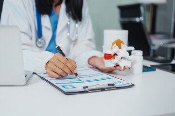 Asian female doctor uses a model of a lumbar disc to work with a computer, plans treatment,...