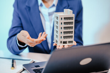 A female employee works at her desk in a real estate office, managing condo sales in the city. She...