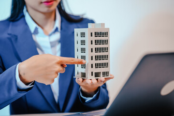 A female employee works at her desk in a real estate office, managing condo sales in the city. She...