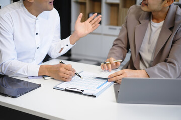 Two Asian businessmen sit in the office using laptops. They manage business tasks, communicate with...