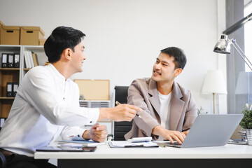 Obraz premium Two Asian businessmen sit in the office using laptops. They manage business tasks, communicate with clients, analyze data, and oversee projects to ensure success and efficiency in their operations
