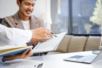 Two Asian businessmen sit in the office using laptops. They manage business tasks, communicate with clients, analyze data, and oversee projects to ensure success and efficiency in their operations