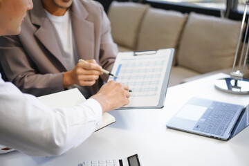 Two Asian businessmen sit in the office using laptops. They manage business tasks, communicate with clients, analyze data, and oversee projects to ensure success and efficiency in their operations