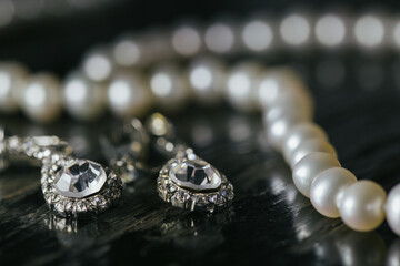 Close-Up of Pearl Necklace and Diamond Earrings on Black Surface

