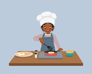 Cute little African girl chef cooking delicious fried egg with frying pan in the kitchen
