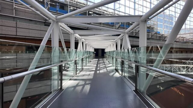 Empty elevated walkway made of glass and steel inside Tokyo International Forum, point of view of someone walking