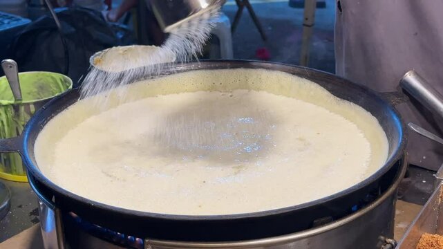 A close-up of a vendor making large peanut pancakes, aka apam balik, on a hawker street food stall at a pasar malam in SS2, Petaling Jaya, Malaysia