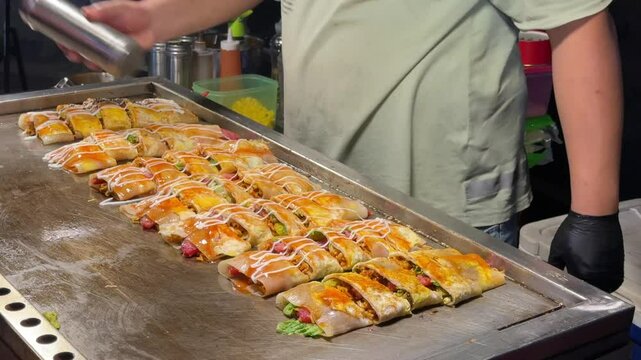 A close-up of a vendor making crispy popiah and pancake rolls on a hawker street food stall in Penang, Malaysia