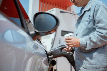 Man refuels car while holding a beverage at a modern gas station in bright daylight
