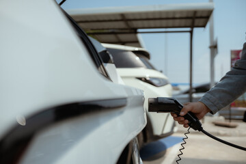 Person charging an electric vehicle at a charging station on a sunny day in a green outdoor setting