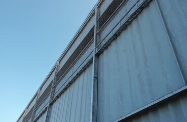 Obraz premium Low angle shot of industrial building cladding with expanded metal lattice structure, galvanized gray nets protect silver metal facade, against blue sky. Wall corner slanted sheet shows urban