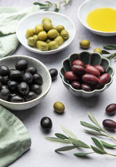 Bowls of black, green and kalamata olives with olive oil and olive branches on marble table