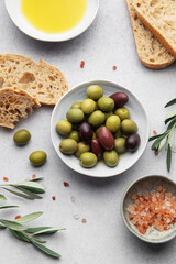 Green and black olives with olive oil, bread and himalayan pink salt on grey table