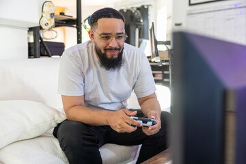 A young man is immersed in the enjoyment of playing a captivating video game at home, which...