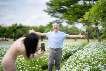 Fototapeta premium Oldery Asian man enjoy relaxing moment with fresh air and nature with her daughter. Senior retired man open arm for take a photo. Healthy retirement travel and life insurance concept.