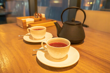 A warm and inviting tea setup featuring two elegant white cups filled with tea, placed on a wooden table. A black cast iron teapot sits nearby, adding a touch of traditional charm. 